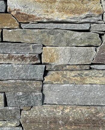 Kit dry stack ledgestone natural stone veneer closeup showing earth tone grey, red, and brown chipped stone texture.