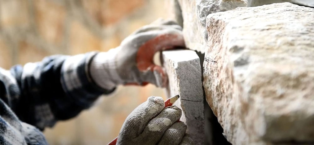Stone mason wearing gloves marking where a piece of natural stone veneer needs to be cut