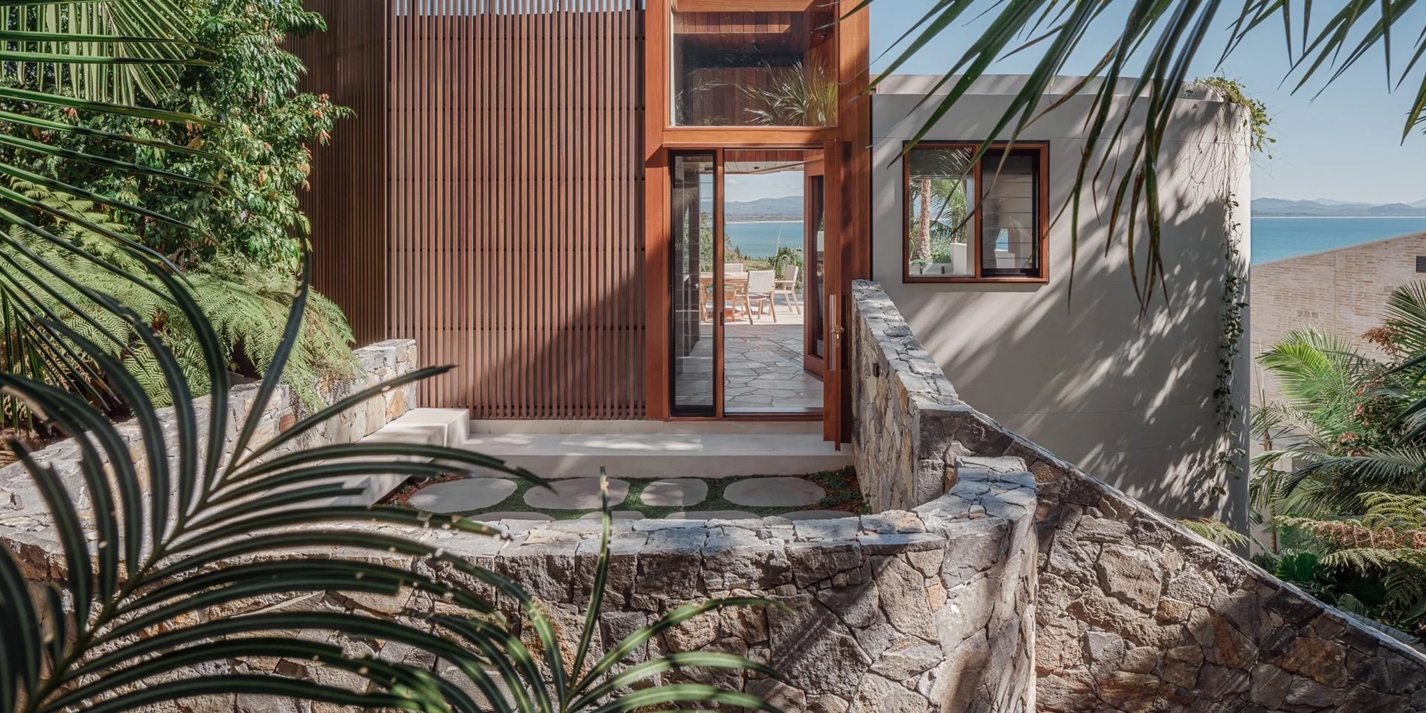 Costa TerraForm natural stone veneer retaining wall on a modern hillside entry with tropical landscaping and ocean views