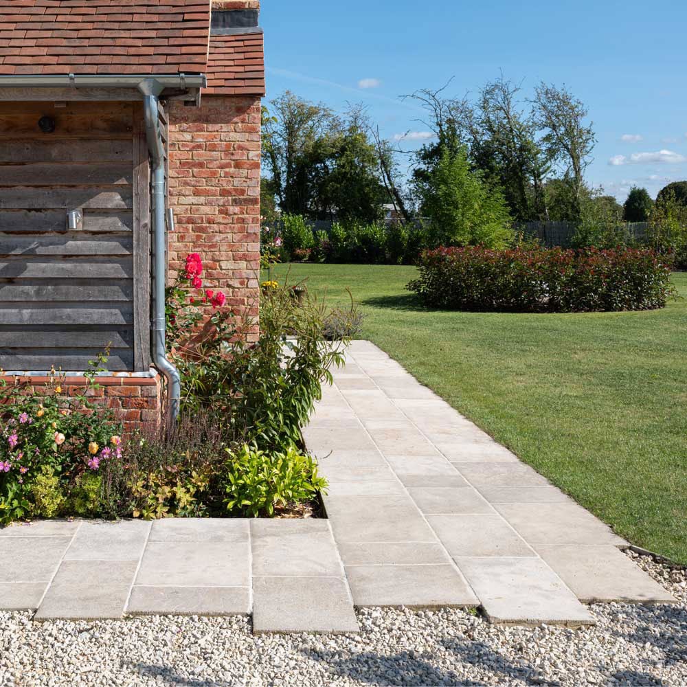 Free length sandstone flooring on an outdoor patio and garden walkway beside a brick and timber home