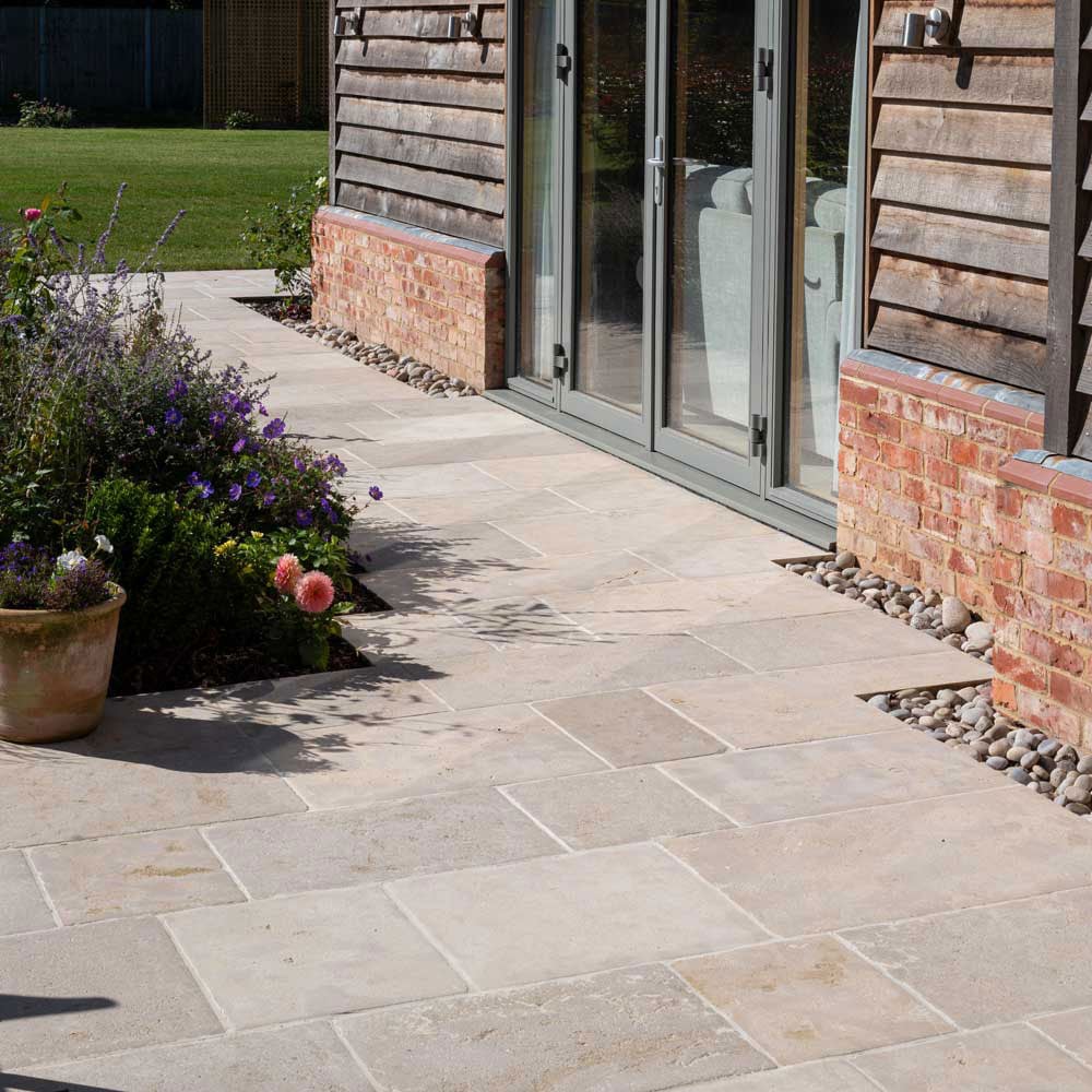 Sandstone exterior stone flooring installed beside a brick home with planting beds and a natural stone walkway