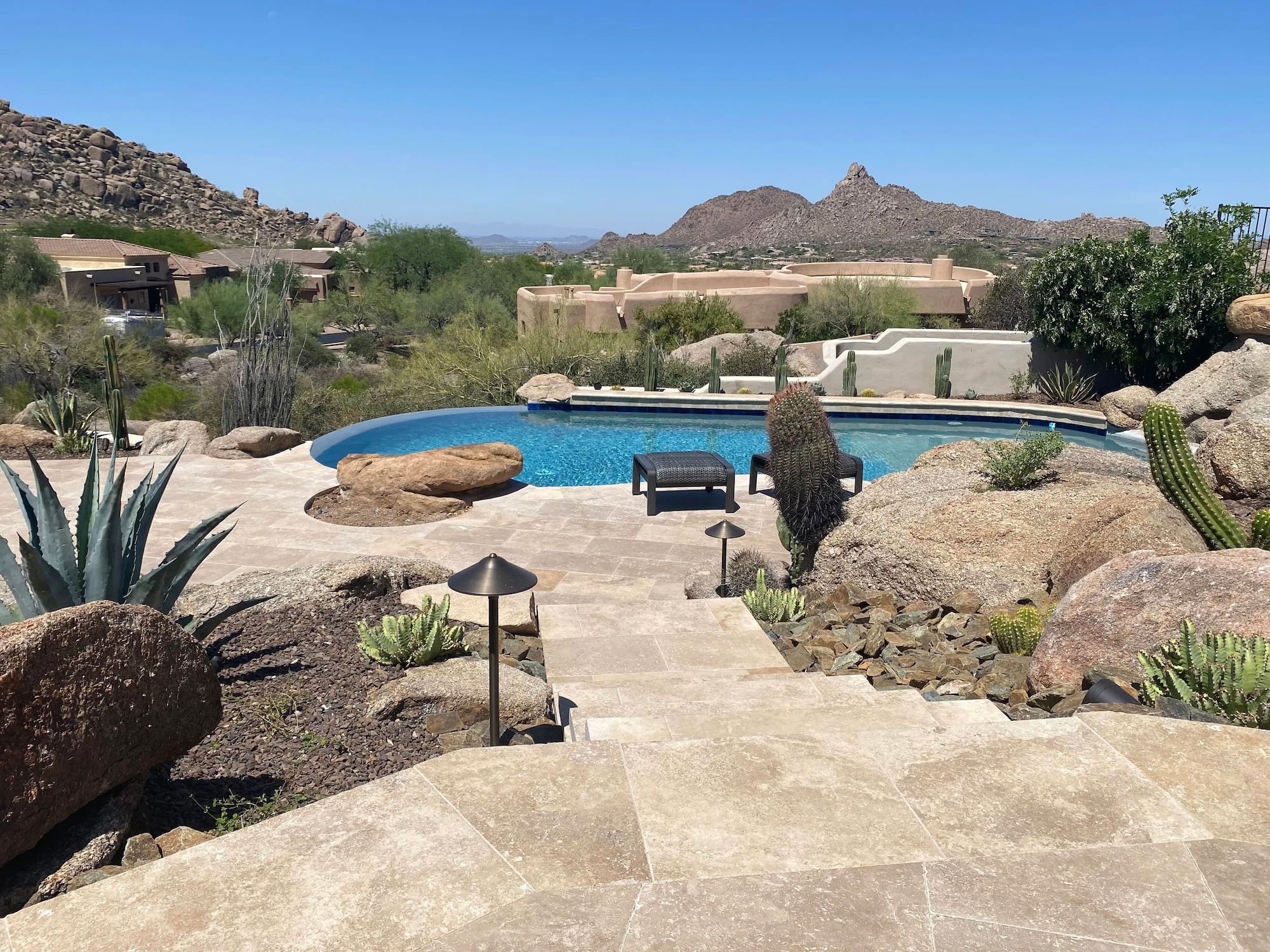 Travertine natural stone paver steps and pool deck in a desert landscape with cacti, boulders, and mountain views