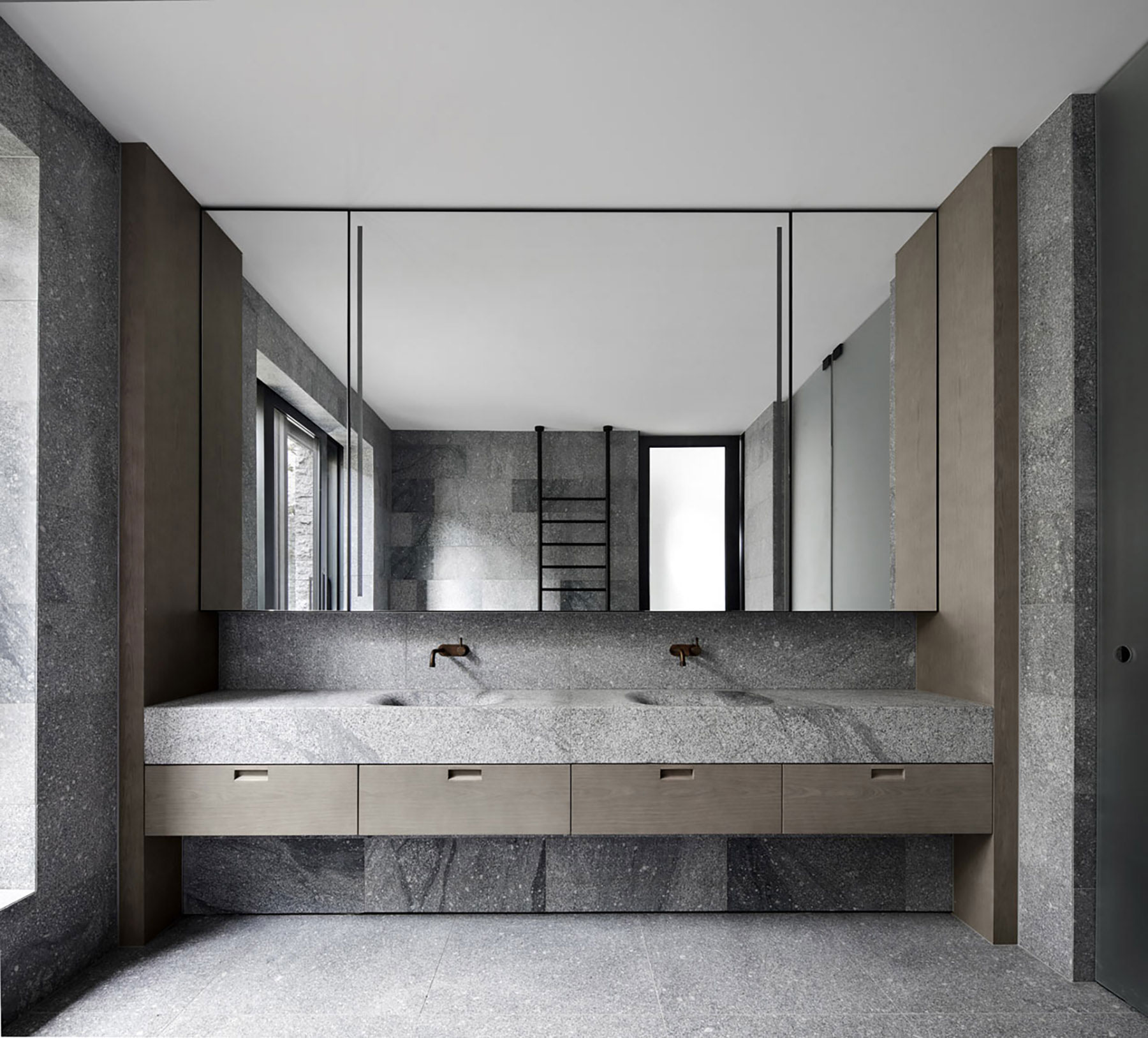 Durable granite interior flooring in a modern bathroom with matching stone walls, floating vanity, and large mirrored cabinets
