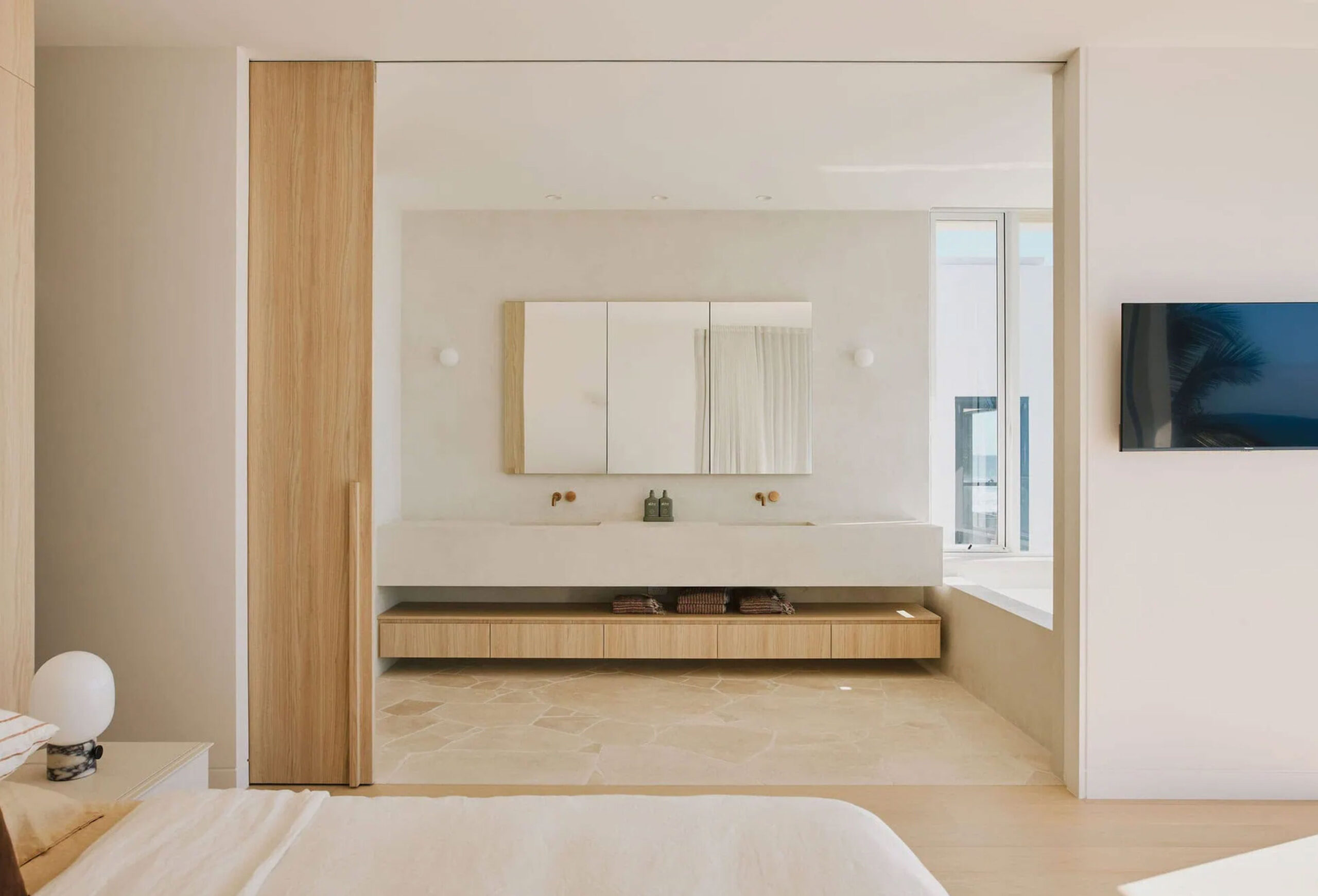 Interior irregular travertine bathroom floor in a bright modern suite with warm wood cabinetry and a floating vanity