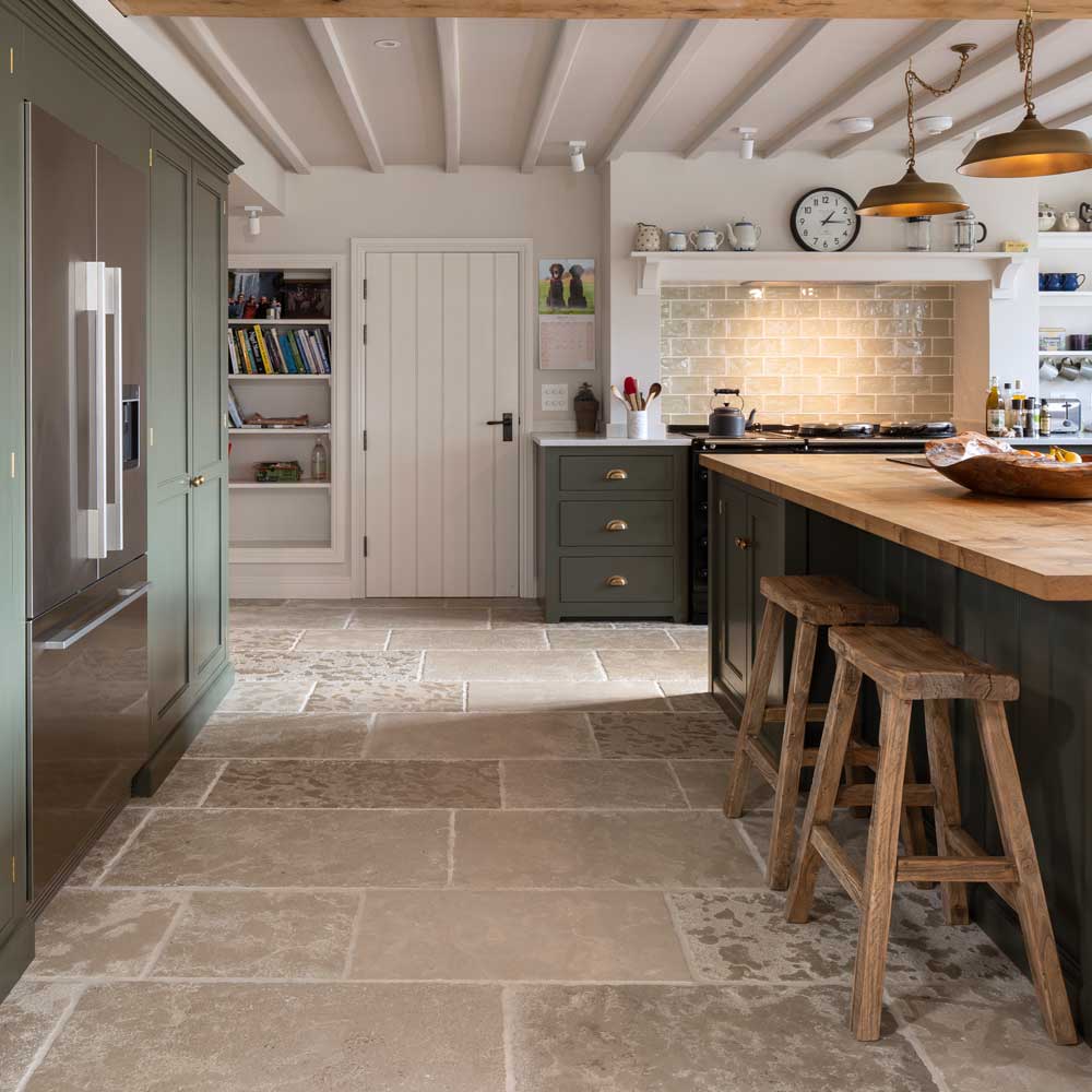 Sandstone flooring in a rustic kitchen with warm neutral stone tiles, green cabinetry, and wood accents