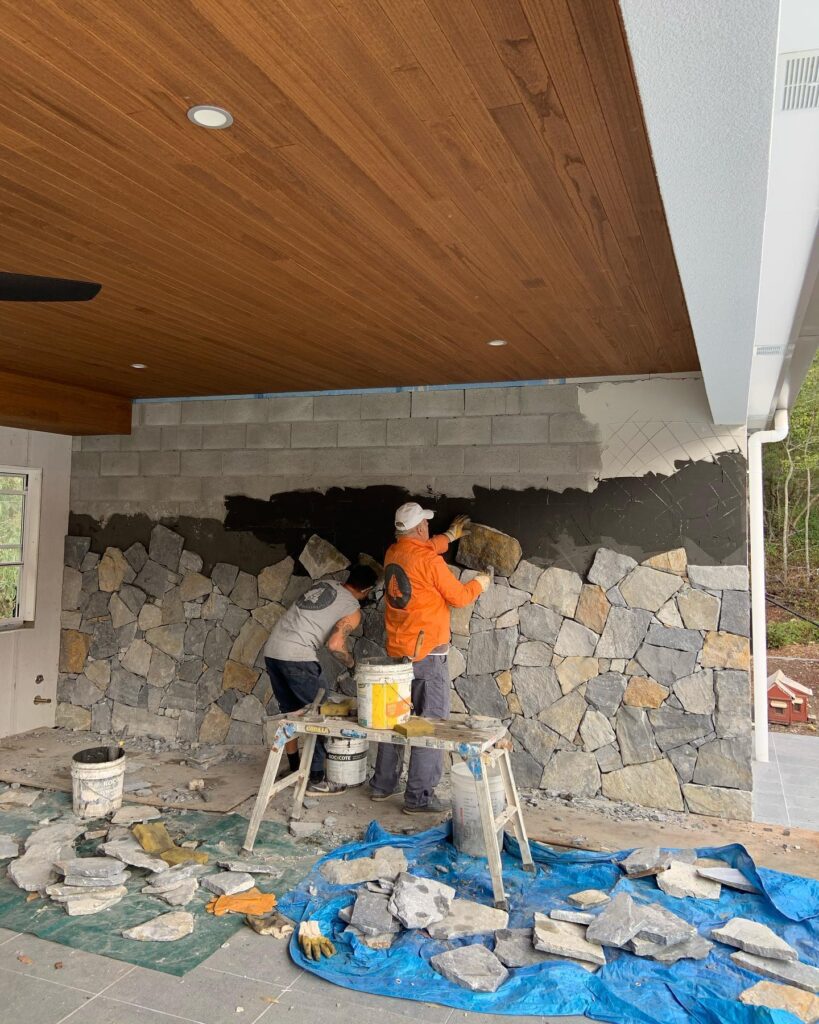 Installing final rows of irregular stone veneer on an exterior wall